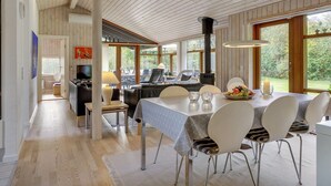 A spacious dining area with a high ceiling and wooden beams, a central table with chairs, and a view of the outdoors through large windows.