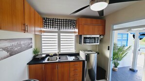 Una cocina compacta con armarios de madera, encimera negra, refrigerador de acero inoxidable y microondas.