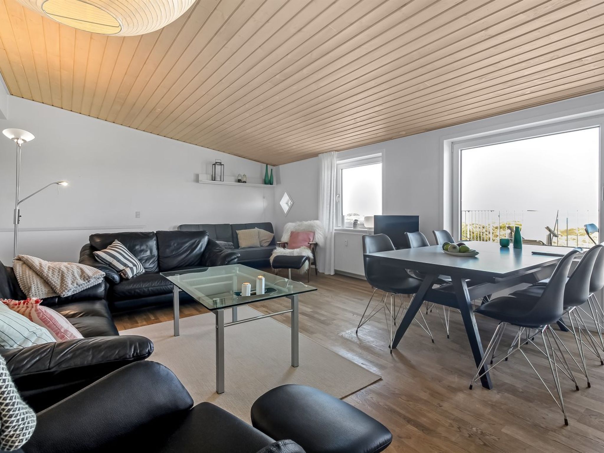 Un salon moderne avec une table basse en verre, un canapé en cuir noir et un coin repas comprenant une table et des chaises.
