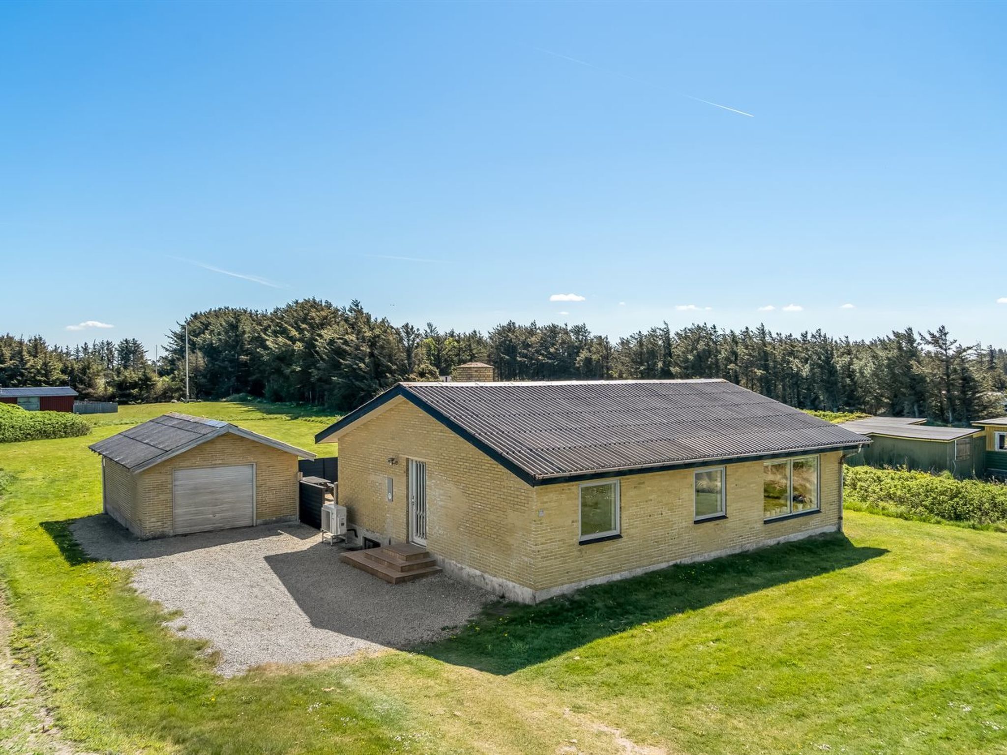 Une maison de plain-pied en briques, avec un toit en pente, un garage et un petit abri attenant.
