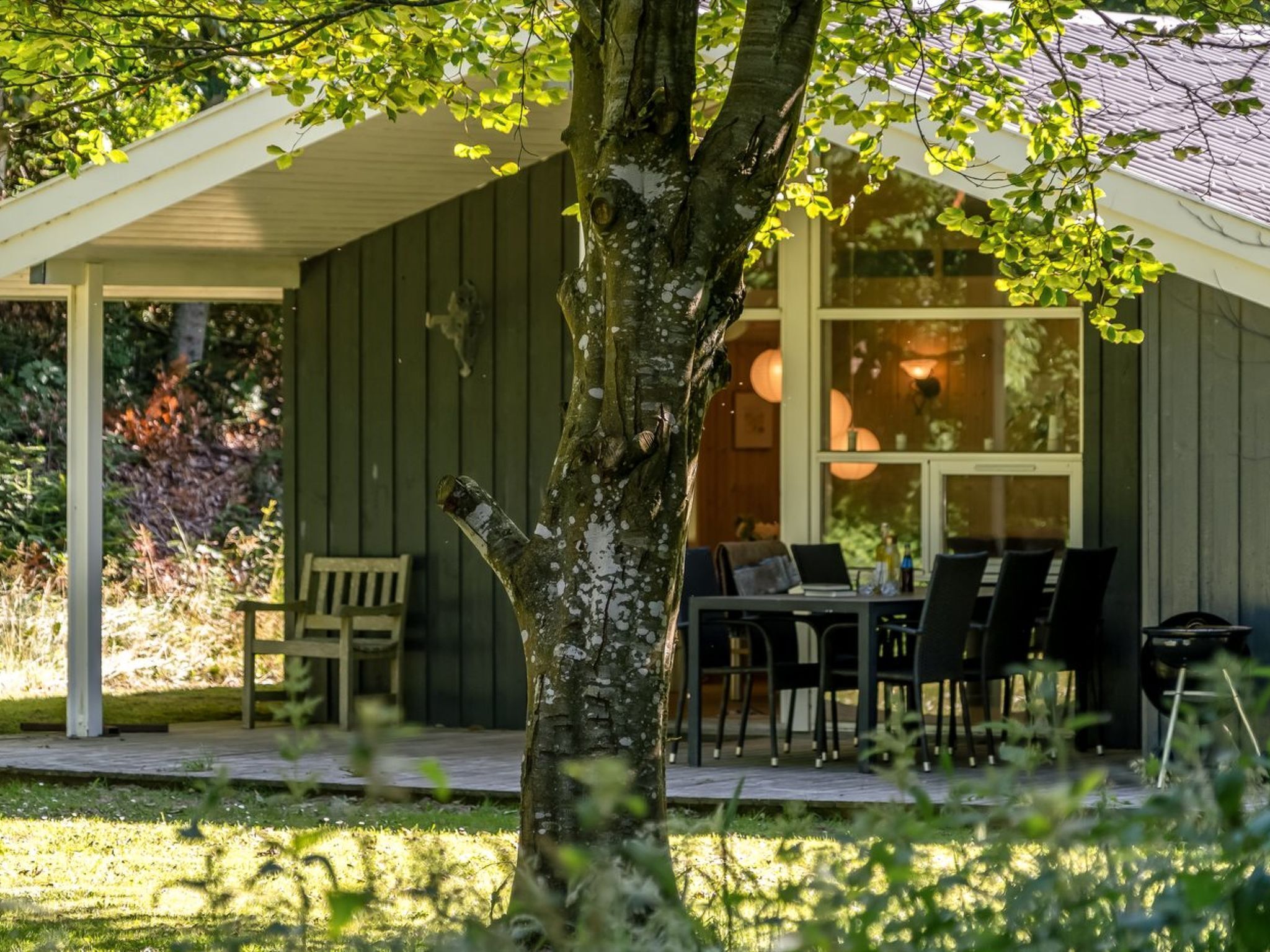 Een gezellig buiten eetgedeelte met een tafel, stoelen, een houten bank en een boom op de voorgrond.