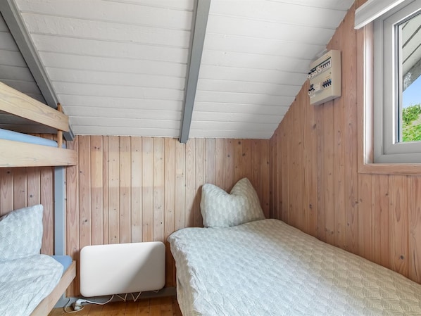 Ein kleiner Raum mit Holzwänden, Stockbetten, einem Einzelbett und einem weißen Nachttisch.