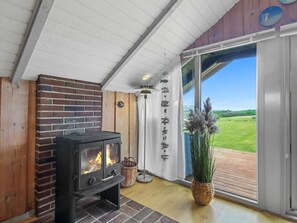 Ein gemütliches Zimmer mit Kaminofen, großem Fenster und Blick ins Grüne.
