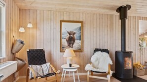 A cozy room with wooden walls, a black stove, two chairs, a table, and a framed picture of a bull. - "Gerhild" - 300m from the sea by Interhome (Ebeltoft)