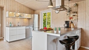 A modern kitchen with wooden paneling, a central island with bar stools, and a window providing a view of greenery. - "Gerhild" - 300m from the sea by Interhome (Ebeltoft)