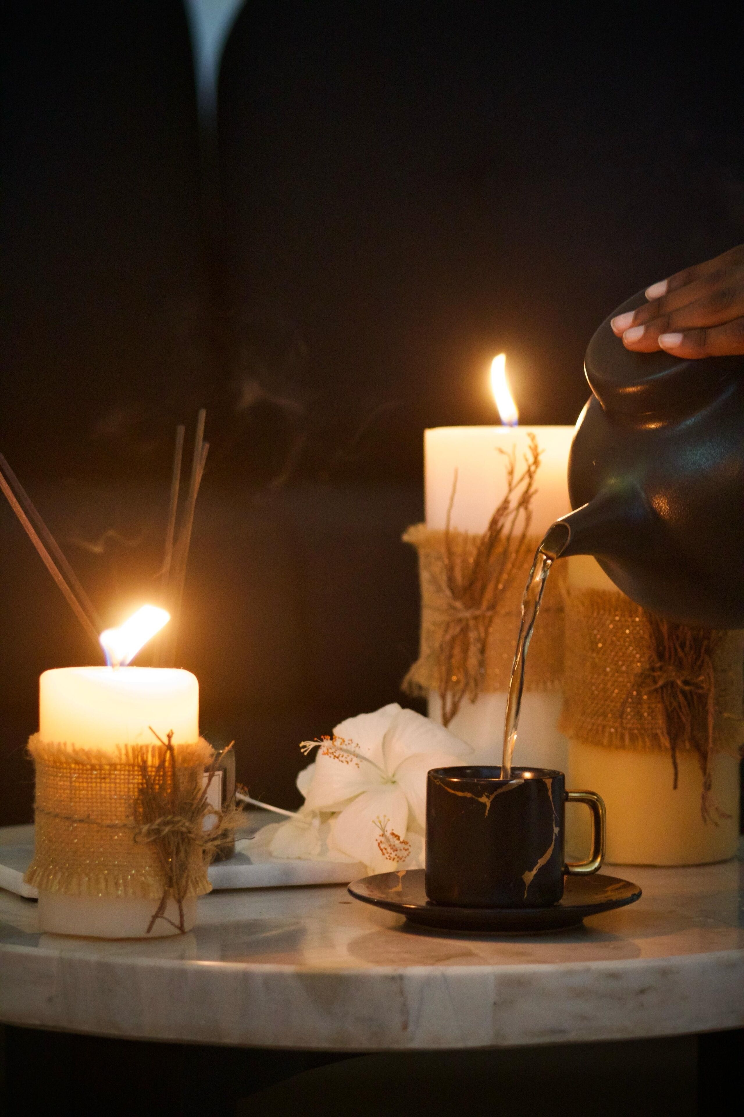 A candlelit table with a candle, a mug, and a pitcher pouring liquid.