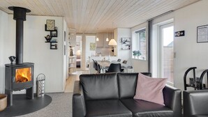 Een gezellige woonkamer met een open haard, een zwarte leren bank en een eethoek met een tafel en stoelen.