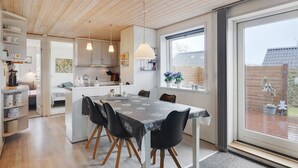 Een moderne keuken met houten plafond en witte kasten, een eethoek met een marmeren tafel en zwarte stoelen, en een grote schuifdeur die uitkomt op een tuin.