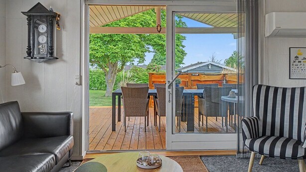 Een kamer met een schuifdeur naar een terras, een zwarte leren bank, een gestreepte fauteuil en een klok aan de muur.