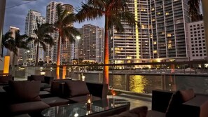 A waterfront hotel with outdoor seating, palm trees, and high-rise buildings in the background. - Luxury Sky Villa w/ City & Ocean Views (Miami)