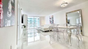 Een moderne eethoek met een glazen tafel en stoelen, een witte bank en een grote spiegel.