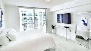Een moderne hotelkamer met een groot bed, een televisie, een bureau en een balkon met uitzicht op de stad.