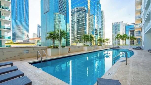 Una piscina con sillas de descanso, rodeada de edificios altos.