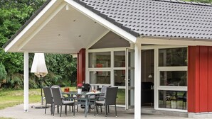 Een overdekt terras met een eettafel, stoelen, een bloempot en een lamp.