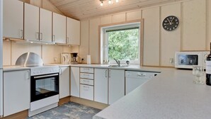 Een moderne keuken met witte kasten, een inbouwoven, een koffiezetapparaat en een raam met uitzicht op groen.