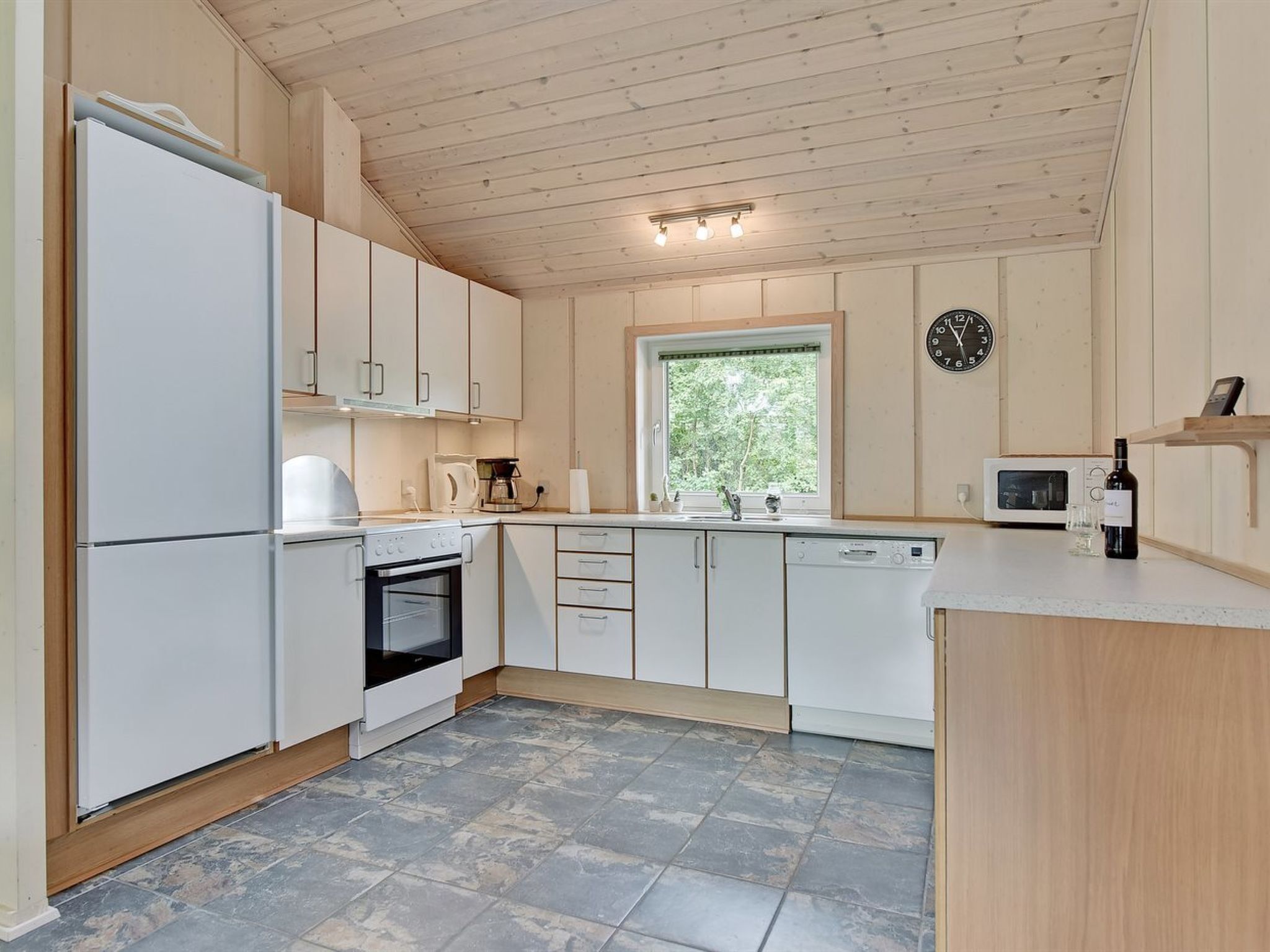 A modern kitchen with white cabinets, a built-in oven, a microwave, and a window with a view of greenery.