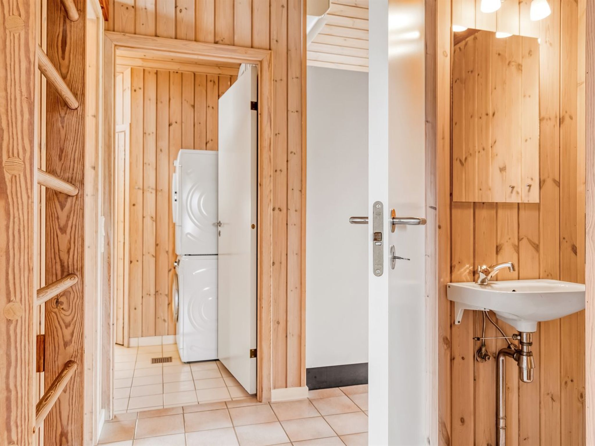 Interior de madera con una puerta blanca que da a una habitación con un refrigerador blanco.