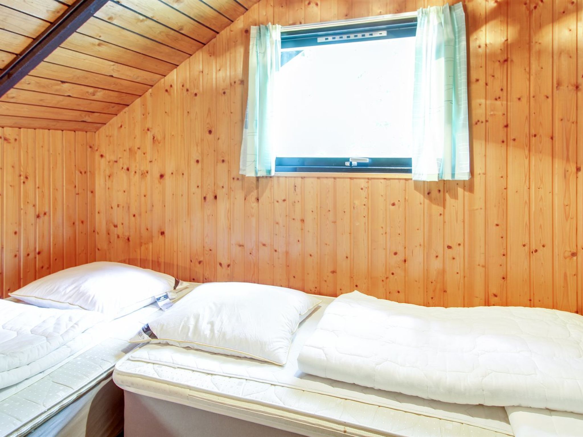 Une chambre avec deux lits, des murs en bois, une fenêtre avec des rideaux et un thermostat visible.