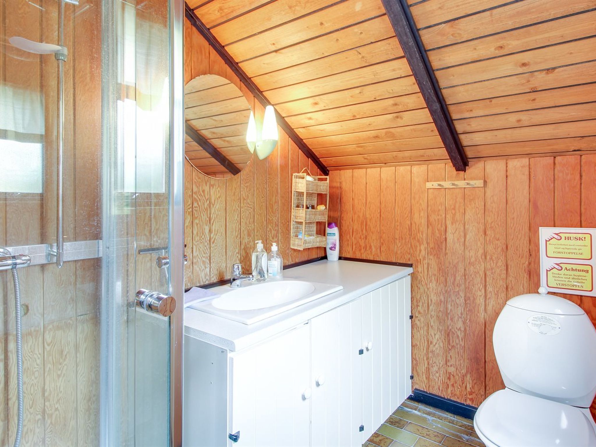 Une salle de bain aux murs lambrissés, équipée d’une douche, de deux lavabos et de toilettes.