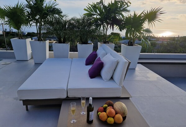 A rooftop terrace with a white sofa, two glasses of wine, and a fruit bowl.