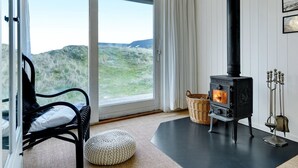 Et hyggeligt rum med en sort brændeovn, en fletkurv, en polstret bænk og udsigt til det fri.