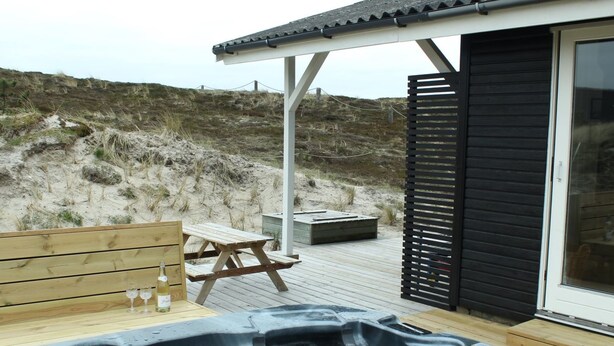 En træterrasse med jacuzzi, picnicbord og et glasindhegnet rum.
