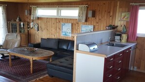 Ein gemütliches Blockhaus-Interieur mit Holzausstattung, einer Couch, einem Couchtisch, einer Küchenzeile mit Spüle und Toaster sowie einem Fenster mit Vorhängen.