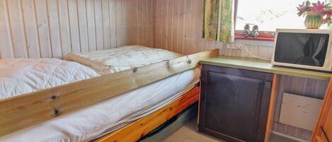 Una habitación compacta con una cama litera, un escritorio pequeño con un microondas y una ventana con cortinas.