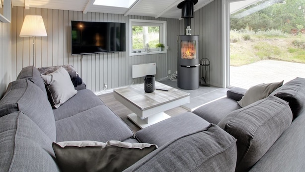 A modern living room with a grey sofa, a flat-screen TV, a fireplace, and a skylight.