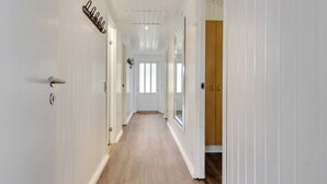 A long, narrow hallway with white walls and wooden flooring, leading to a door with a wooden panel.