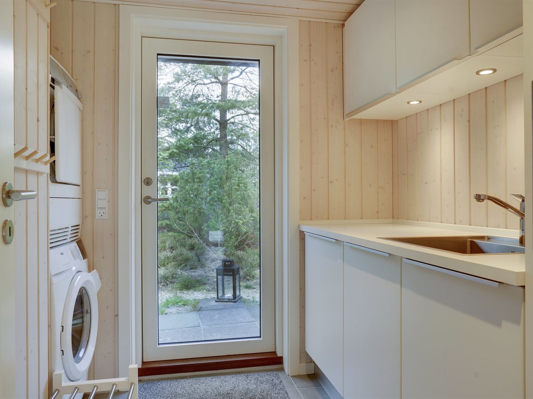 Une salle de bain moderne et compacte, dotée d’un lave-linge et d’un sèche-linge intégrés, d’un lavabo et donnant sur un jardin grâce à une porte vitrée.