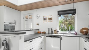Une cuisine moderne avec des meubles blancs, un lave-vaisselle, un four encastré et une fenêtre donnant sur la verdure.