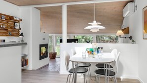 Une cuisine moderne avec un coin repas, comprenant une table blanche avec quatre chaises, un luminaire suspendu et une vue sur la verdure à l’extérieur.