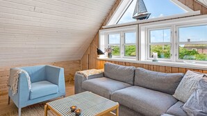 A cozy room with a sloped ceiling, wooden walls, a sofa, a chair, and a table with candles.