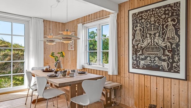 A dining area with a wooden table, white chairs, pendant lights, and a large framed artwork on the wall.