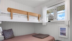 A small, single-bed room with a bunk bed above, a window with a view, a bedside table, and a framed picture on the wall.