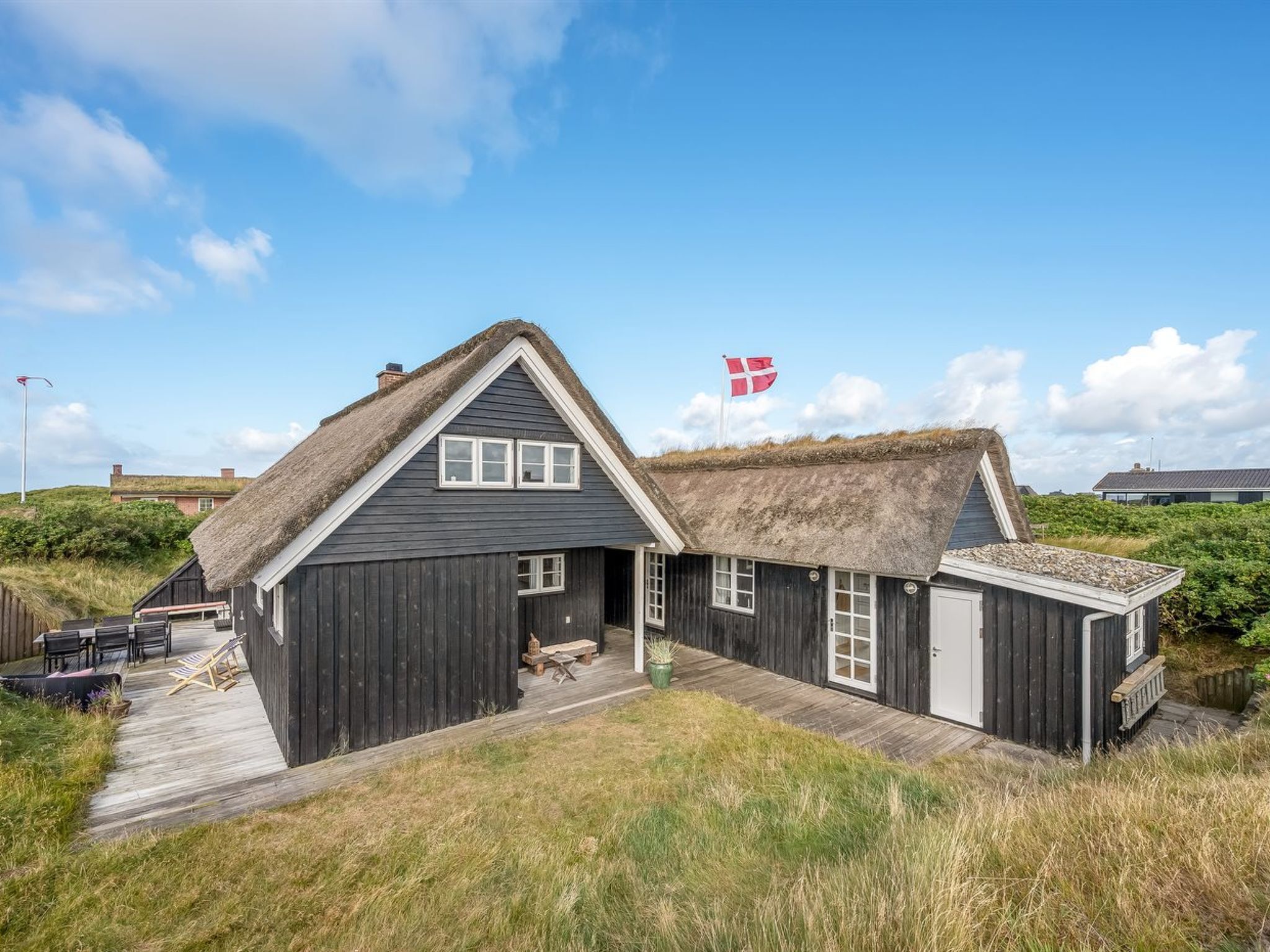 A thatched-roof house with a flag, wooden deck, and outdoor seating.