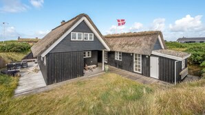 A thatched-roof house with a flag, wooden deck, and outdoor seating.