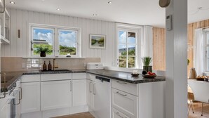 A modern kitchen with white cabinetry, a granite countertop, and a view of the outdoors through large windows.