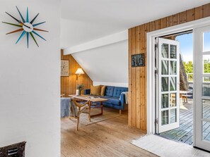 Una habitación acogedora con techo de madera, un sofá azul, una mesa de comedor de madera y un ventanal grande.
