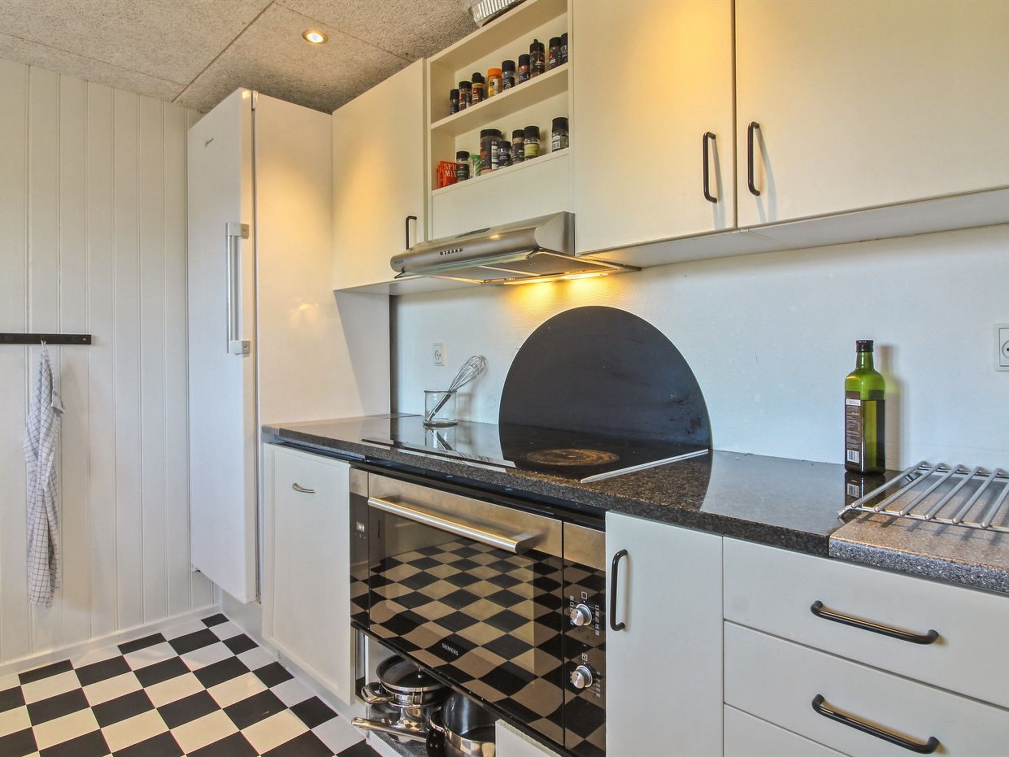 A kitchen with a checkered floor, a built-in oven, a spice rack, and a hanging towel.