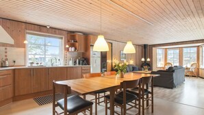 Eine moderne Küche mit Holzausstattung, ein Essbereich mit Holztisch und -stühlen sowie ein Wohnbereich mit einer Couch und Sesseln.