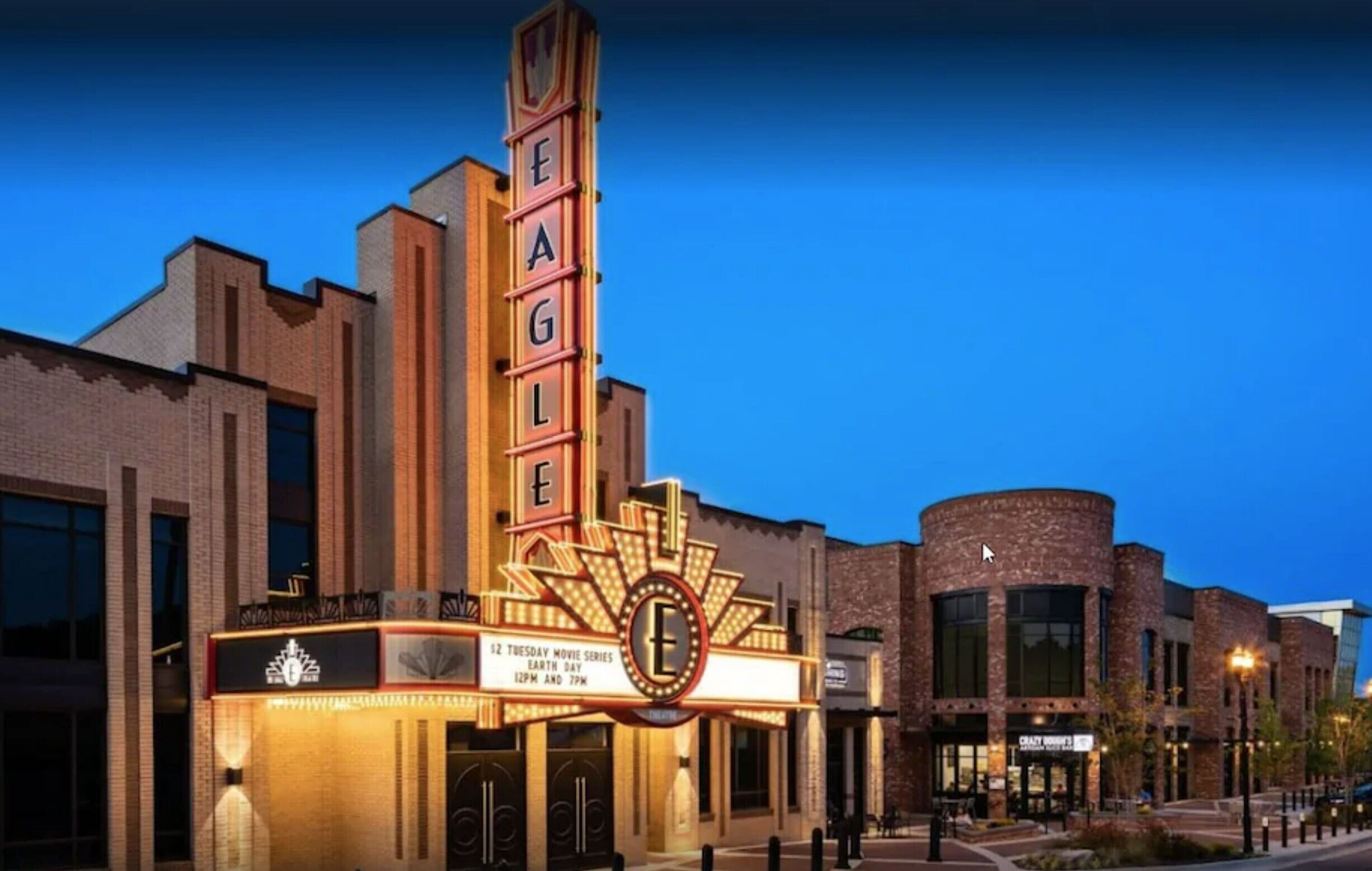 A theater with a prominent marquee displaying "EAGLE" and a sign indicating movie series on Tuesdays.