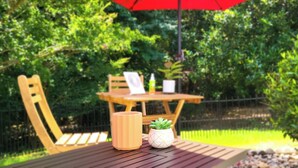 Et træbord med rød parasol, en potteplante og et stearinlys.
