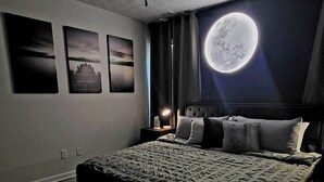 A bedroom with a large bed, a bench, and a wall-mounted moon decoration. - Enchantress Lake Cottage - KING BED/SLEEPS 10 (Buford)