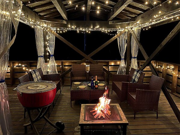 Una terraza al aire libre con mobiliario de mimbre, una parrilla roja y una chimenea.