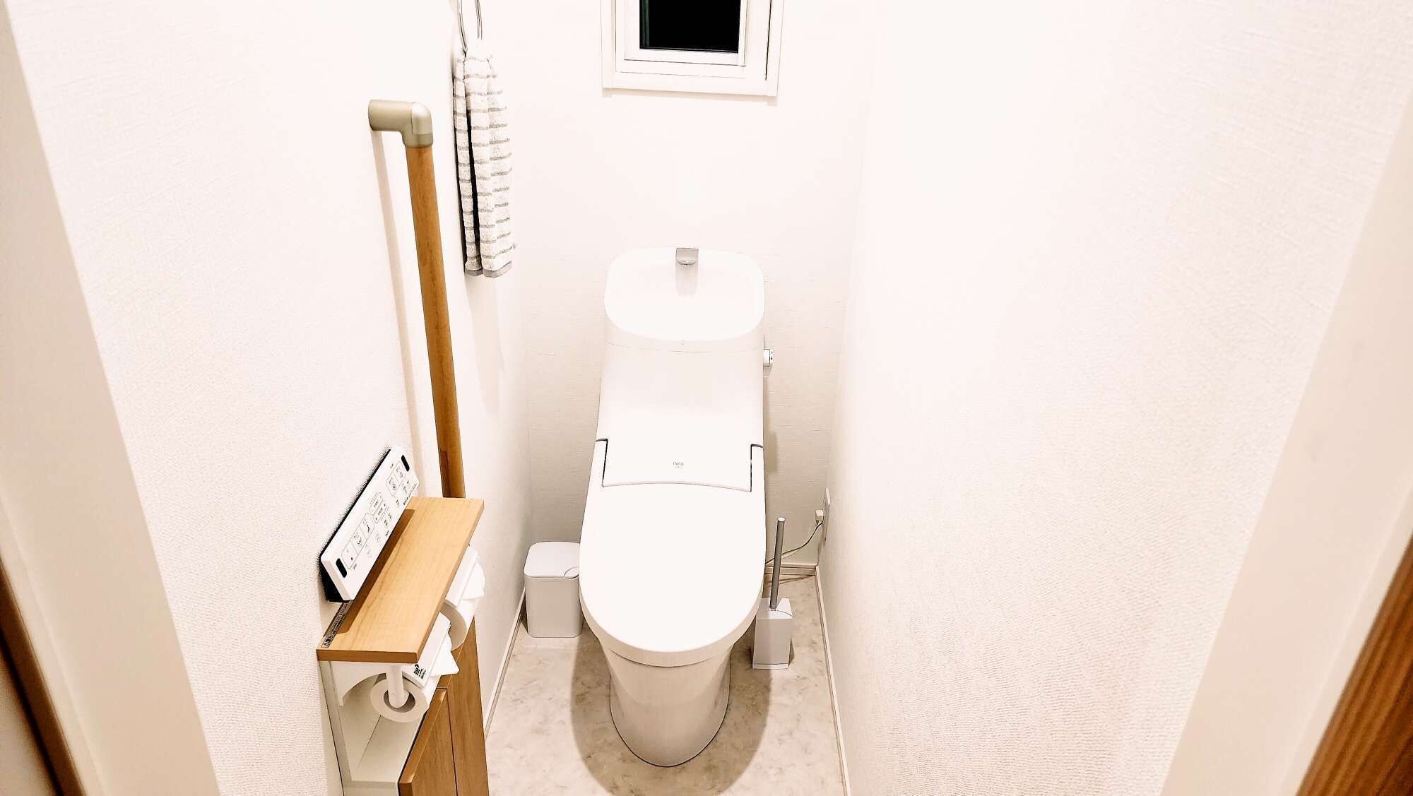 A small, compact bathroom with a toilet, a wooden shelf, and a towel hanging on a rack.