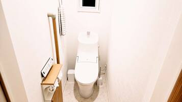 A small, compact bathroom with a toilet, a wooden shelf, and a towel hanging on a rack.