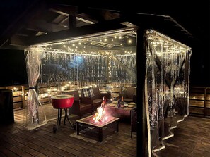 Un espacio al aire libre con un patio, luces colgantes, un brasero y mobiliario de mimbre.
