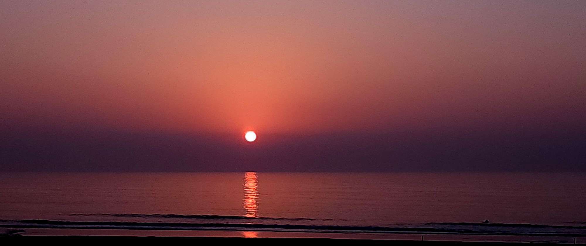 A sunset over a calm sea with a beach in the foreground.